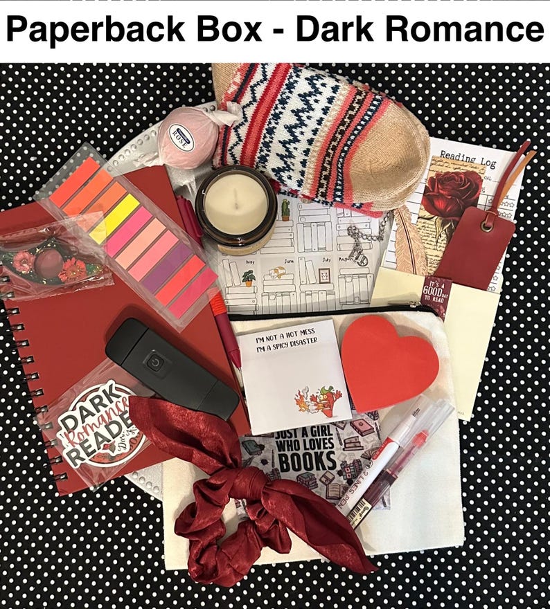 May include: A curated "Dark Romance" themed gift box with a red notebook, candle, socks, and other accessories. Includes a bookmark, sticky notes, and a scrunchie. The box is filled with items for book lovers.