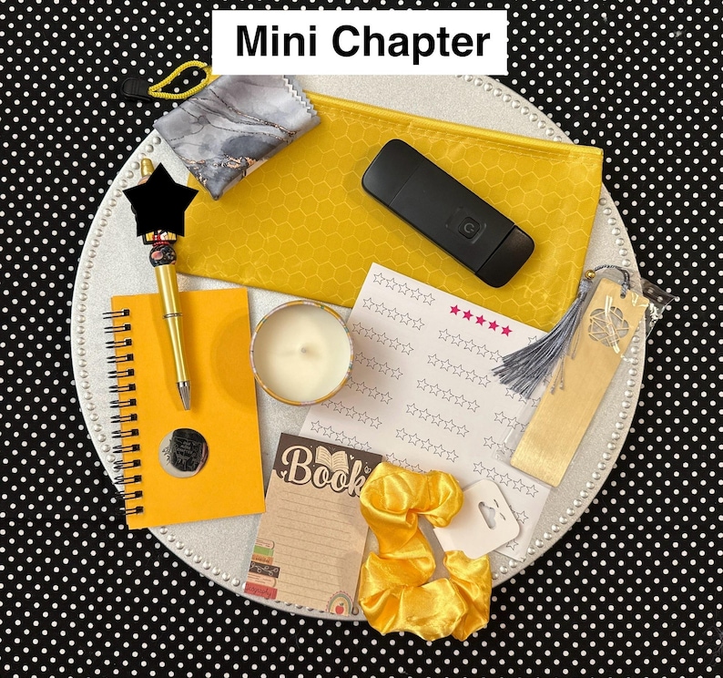 May include: A collection of stationery items, including a yellow spiral notebook, pen, candle, bookmark, and scrunchies. The items are arranged on a white plate with a black and white polka dot background. The text "Mini Chapter" is at the top.