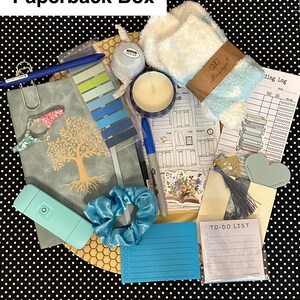 May include: A curated gift box with a variety of items. Includes a journal, pen, candle, scrunchie, notepad, and other stationery items. The box is on a black and white polka dot background. The text "Paperback Box" is at the top.
