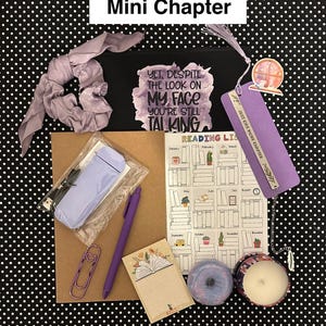 May include: A collection of reading-themed items, including a black pouch with text, a bookmark, a pen, a notebook, a candle, and a scrunchie. The items are arranged on a black and white polka dot background. The pouch reads "YET, DESPITE THE LOOK ON MY FACE YOU'RE STILL TALKING."