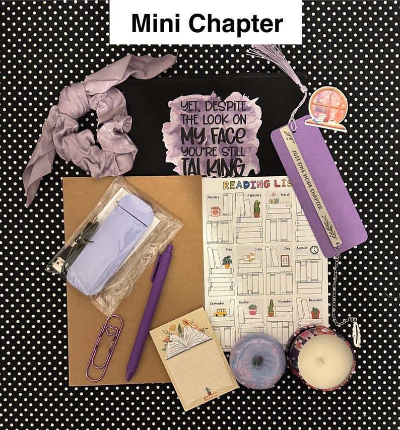 May include: A collection of reading-themed items, including a black pouch with text, a bookmark, a pen, a notebook, a candle, and a scrunchie. The items are arranged on a black and white polka dot background. The pouch reads "YET, DESPITE THE LOOK ON MY FACE YOU'RE STILL TALKING."