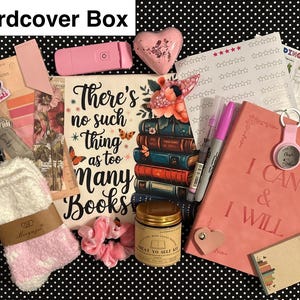 May include: A curated gift box with a variety of items. Includes a pink journal with "I CAN & I WILL" text, a book-themed sign, a jar, socks, and other accessories. The box is on a black and white polka dot background.