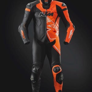 May include: Black and orange motorcycle racing suit with the KTM logo. The suit features a combination of black and orange panels, with white accents and protective padding on the knees and elbows. The suit is designed for safety and performance.