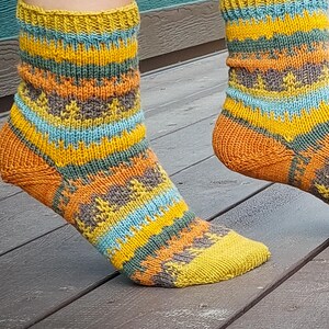 May include: A pair of knitted socks with a vibrant colour scheme. The socks display a pattern of horizontal stripes in yellow, orange, blue, and grey. The socks are worn, with the toes and heels in yellow and orange.