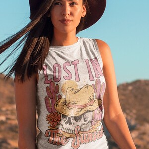 Peut inclure: Un d&eacute;bardeur blanc avec un imprim&eacute; graphique d'un cr&acirc;ne portant un chapeau de cowboy et entour&eacute; de cactus. Le texte "Lost in the Sunset" est imprim&eacute; sur le d&eacute;bardeur.