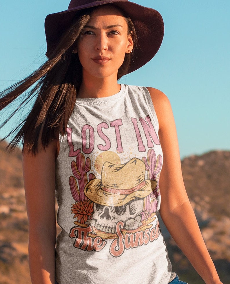 Peut inclure: Un d&eacute;bardeur blanc avec un imprim&eacute; graphique d'un cr&acirc;ne portant un chapeau de cowboy et entour&eacute; de cactus. Le texte "Lost in the Sunset" est imprim&eacute; sur le d&eacute;bardeur.