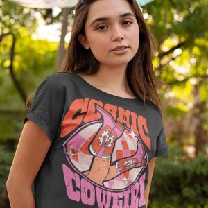 May include: A black cropped t-shirt with a pink and orange graphic of a pair of pink cowboy boots with the text "Cosmic Cowgirl" in pink letters.