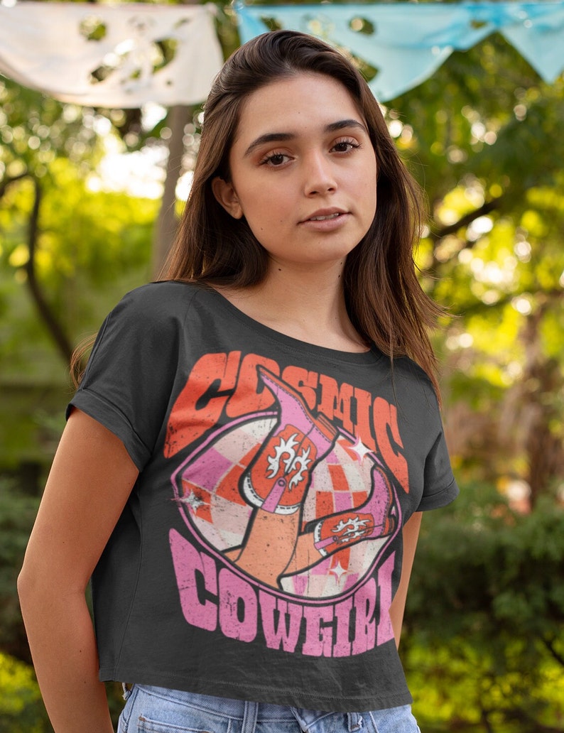 May include: A black cropped t-shirt with a pink and orange graphic of a pair of pink cowboy boots with the text "Cosmic Cowgirl" in pink letters.