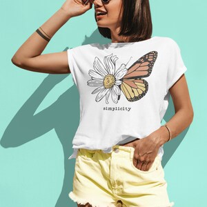 K&ouml;nnte beinhalten: Wei&szlig;es T-Shirt mit einem Motiv einer G&auml;nsebl&uuml;mchen und eines Schmetterlings mit dem Wort "simplicity" darunter gedruckt. Das Model tr&auml;gt eine gelbe Jeans-Shorts und eine Sonnenbrille.