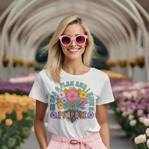 May include: White t-shirt with a floral design and the text "He has a plan and I have a purpose".