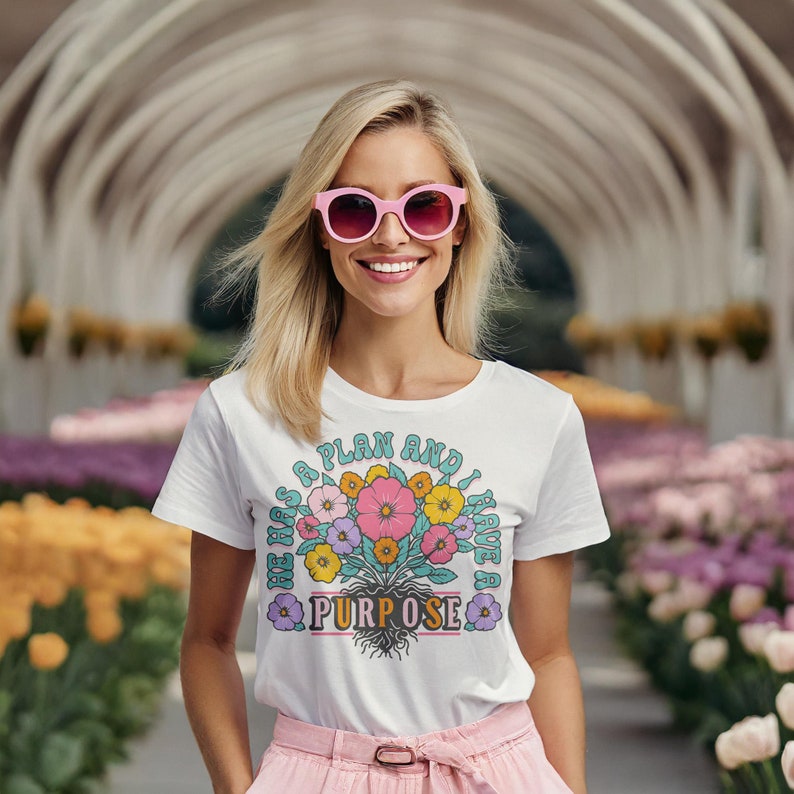 May include: White t-shirt with a floral design and the text "He has a plan and I have a purpose".