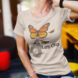 May include: A beige t-shirt with a graphic of a butterfly flying through a stylized musical note. The text "Let Go" is printed below the butterfly.