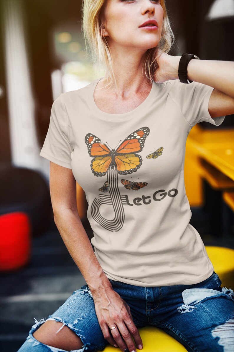 May include: A beige t-shirt with a graphic of a butterfly flying through a stylized musical note. The text "Let Go" is printed below the butterfly.