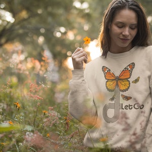 May include: A beige sweatshirt with a graphic of a butterfly and the text "Let Go". The butterfly is orange and black with a white stripe down the middle. The text is in a black font.