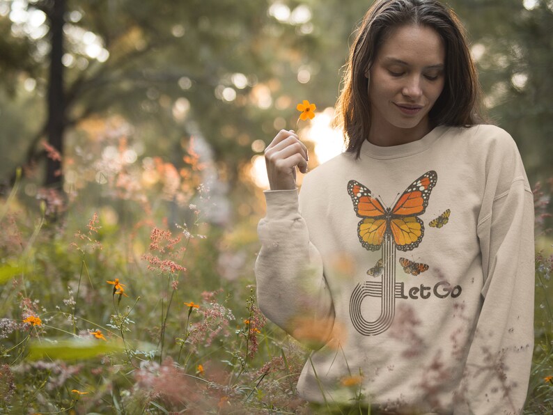 May include: A beige sweatshirt with a graphic of a butterfly and the text "Let Go". The butterfly is orange and black with a white stripe down the middle. The text is in a black font.