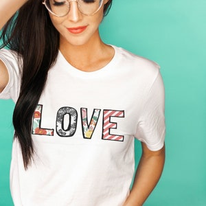 May include: White t-shirt with the word "LOVE" printed in large, colorful letters. The letters are made up of different floral patterns.