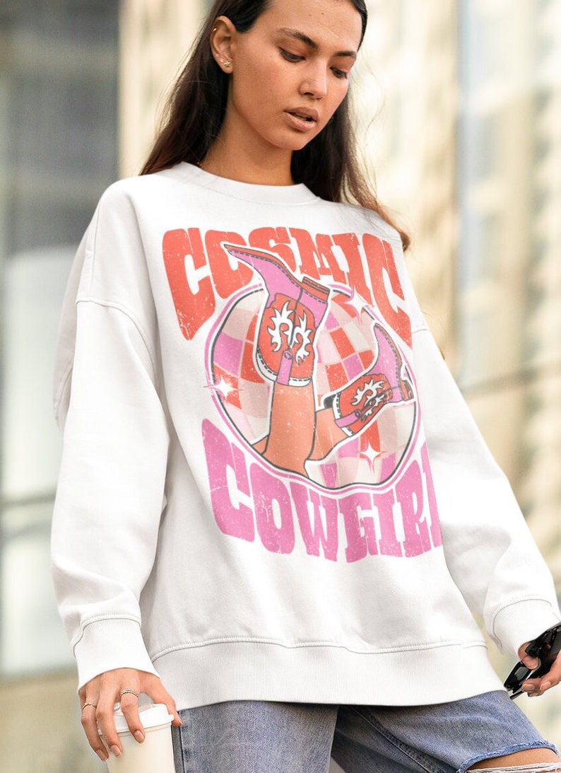 May include: White sweatshirt with a pink and orange graphic print of a woman wearing cowboy boots and the text "Cosmic Cowgirl".