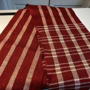 May include: A red and white striped woven fabric with a red and white plaid pattern. The fabric is folded in half and is lying on a white surface.