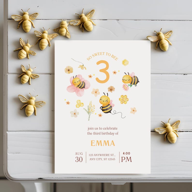 May include: A birthday invitation with the text "So Sweet to Bee" and "3" in orange. The invitation features illustrations of bees and flowers. Decorative bee figurines surround the invitation.