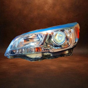 May include: A car headlight with a clear lens and chrome detailing. The headlight features a blue top and an orange side marker. The light is designed with multiple internal reflectors and lenses for optimal illumination.