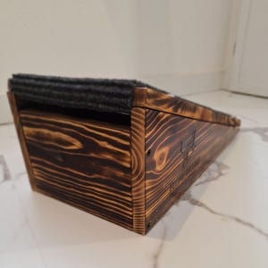 May include: A wooden pet ramp with a dark gray carpeted surface. The ramp is made of stained wood with visible grain and a logo on the side. The ramp is designed to help pets access elevated surfaces.