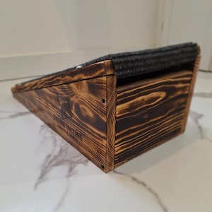 May include: A wooden cat ramp with a dark gray carpeted surface. The ramp is made of stained wood with visible grain and a logo that reads "Feline Incline". The ramp is designed to help cats reach higher places.