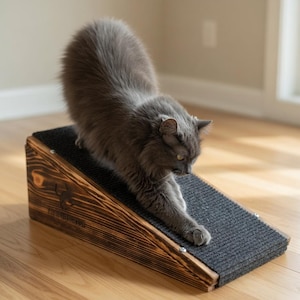 May include: A grey cat stretches on a wooden cat scratcher. The scratcher has a dark grey carpeted surface and a wooden frame with a logo. The cat is stretching its front paws on the scratcher.