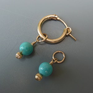 Pode incluir: Um par de brincos de argola de ouro com contas turquesa penduradas neles. Os brincos são simples e elegantes.