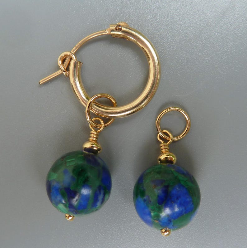 May include: A pair of gold hoop earrings with round, blue and green stone pendants. The earrings have a polished finish and a simple design, suitable for everyday wear. The pendants are approximately 0.5 inches in diameter.