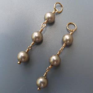 Puede incluir: Un par de pendientes de oro con tres perlas grises en cada pendiente.