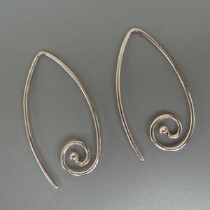 May include: A pair of silver hoop earrings with a swirl design. The earrings are made of thin metal and have a simple, elegant look.