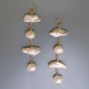 Puede incluir: Un par de pendientes largos de tono dorado con perlas barrocas blancas. Cada pendiente tiene tres perlas, dos de las cuales son de forma irregular y una es redonda.