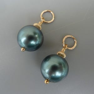 Puede incluir: Dos abalorios de perlas verde oscuro con anillas de salto y detalles dorados. Las perlas son redondas y tienen un acabado liso y brillante.