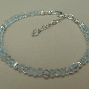 May include: A delicate silver anklet with a chain extender and a row of light blue aquamarine beads.