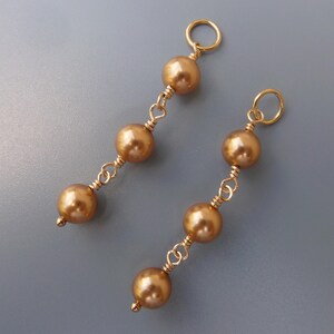 Puede incluir: Un par de pendientes de oro con tres cuentas doradas en cada pendiente.