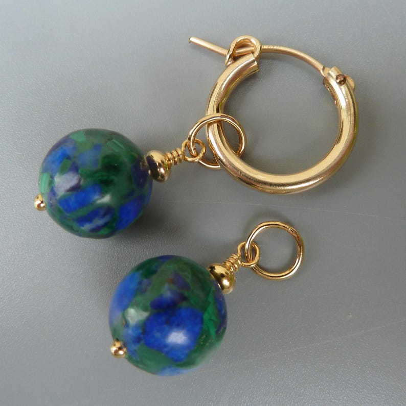 May include: Gold hoop earrings with round, blue and green stone beads. The earrings have a simple design with a gold-colored metal. The beads have a marbled appearance, with a mix of blue and green colors.