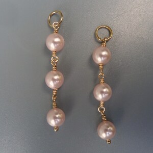 Puede incluir: Un par de pendientes de oro con tres perlas rosadas en cada pendiente.