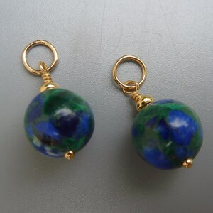 May include: Two round earrings with gold-colored hoops and accents. Each earring features a blue and green marbled stone. The earrings are displayed against a gray background.