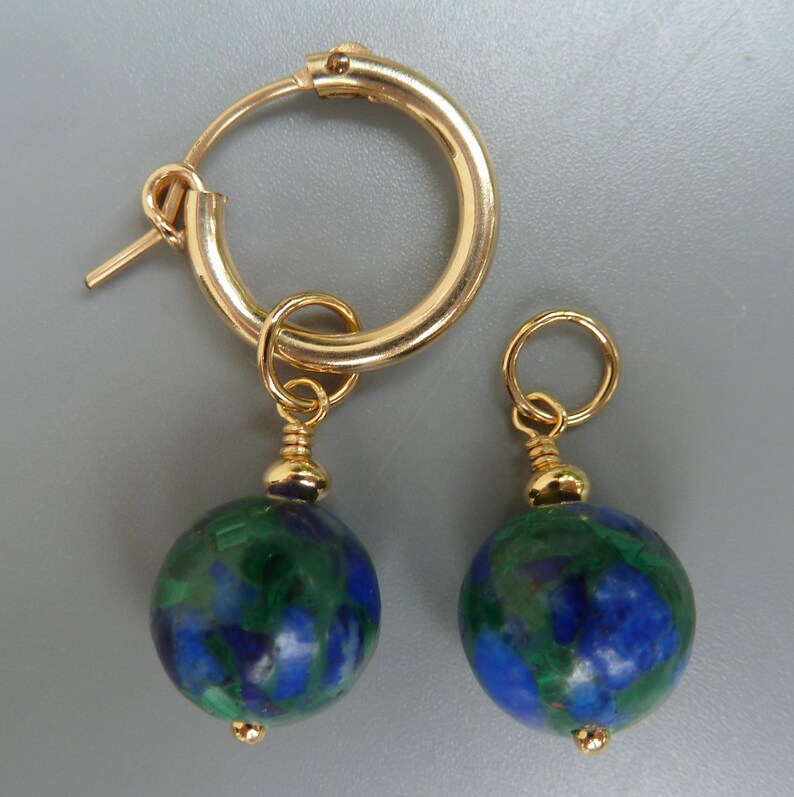 May include: Gold-tone hoop earrings with dangling round beads. The beads are a mix of blue and green, with a gold-tone cap and a small gold bead at the bottom. The earrings are displayed against a gray background.