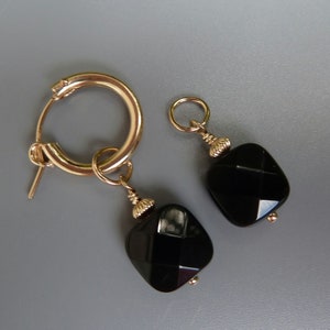 May include: A pair of gold hoop earrings with black square-cut onyx gemstone drops. The earrings have a polished finish and a classic design, suitable for everyday wear or special occasions.
