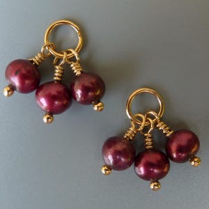 Puede incluir: Dos abalorios dorados con tres perlas de color burdeos colgando de cada abalorio.