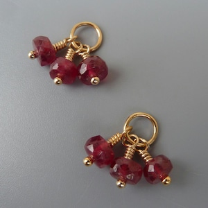 Peut inclure: Une paire de breloques en or avec trois perles de pierres précieuses rouges chacune. Les breloques sont attachées à une boucle en or.