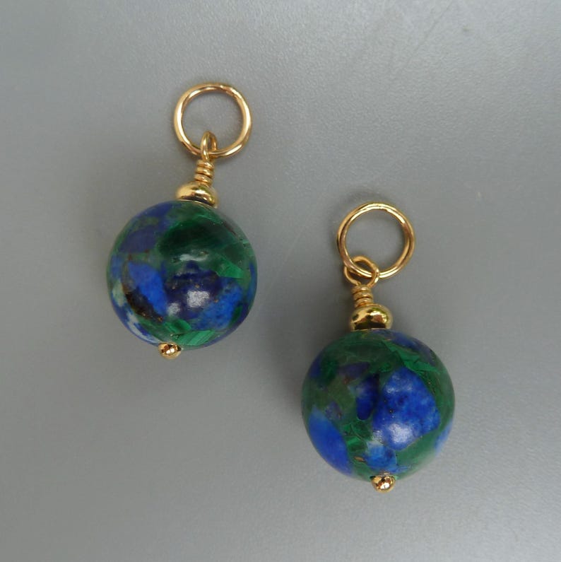 May include: A pair of gold-toned earrings. Each earring features a round, blue and green stone with gold accents. The stones are suspended from a gold loop.