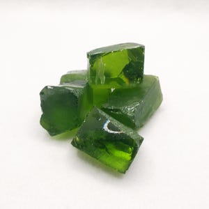 May include: A collection of irregularly shaped, translucent green glass pieces. The glass chunks have a rough, faceted appearance, with varying sizes and shapes. The color is a vibrant, deep green, and light reflects off the surfaces.