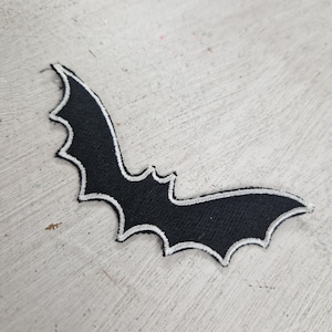 May include: Black felt bat patch with white stitching. The patch is approximately 7.5 cm wide and 5 cm tall.
