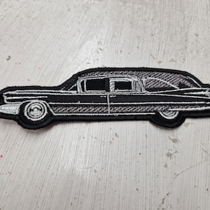 May include: Black and white embroidered patch of a vintage hearse car. The patch is made of fabric and has a stitched outline.