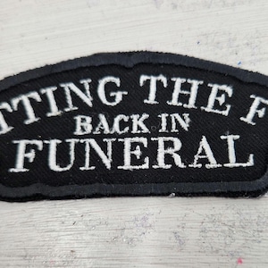 May include: Black and white embroidered patch with the text "Putting the Fun Back in Funeral".