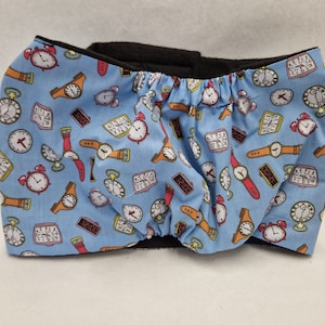 May include: A blue fabric diaper cover with a black elastic waistband. The fabric has a repeating pattern of clocks and watches in various styles.