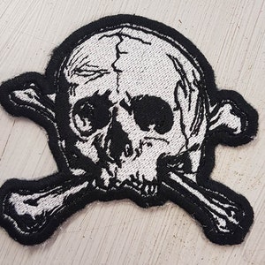 May include: A black and white embroidered patch of a skull and crossbones. The skull is white with black details and the crossbones are black with white details.