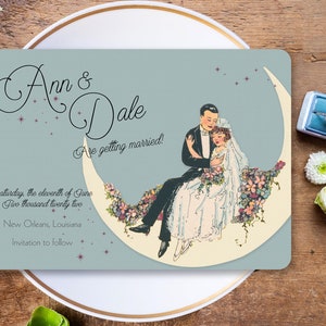 Puede incluir: Una tarjeta de anuncio de boda azul claro con una pareja sentada en una luna creciente. La tarjeta presenta una ilustraci&oacute;n vintage de la pareja con atuendos formales. El texto en la tarjeta dice "Ann & Dale Are getting married! Saturday, the eleventh of June Two thousand twenty two New Orleans, Louisiana Invitation to follow."